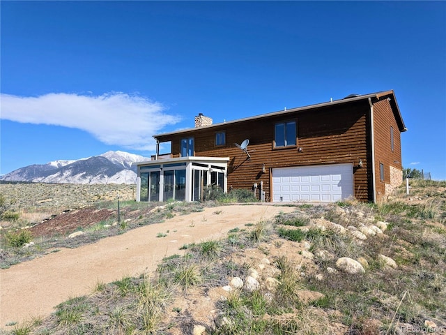 20155 Hideout Ln, Nathrop, CO 81236 - rear view of property featuring a chimney, a mountain view, an attached garage, dirt driveway, and a sunroom