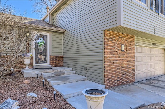 doorway to property with a garage, brick siding, and roof with shingles