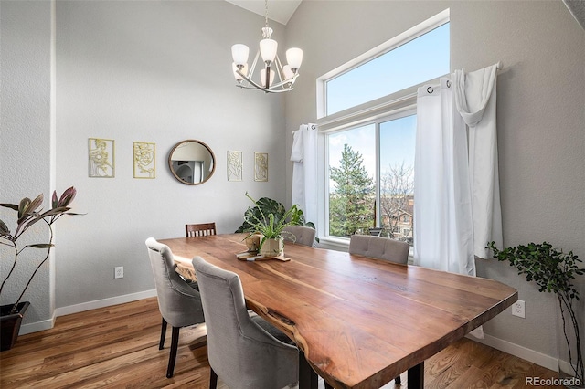 dining space with baseboards, high vaulted ceiling, an inviting chandelier, and wood finished floors