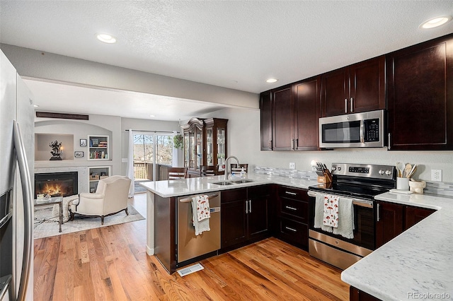 kitchen with a sink, open floor plan, appliances with stainless steel finishes, light wood-style floors, and a peninsula