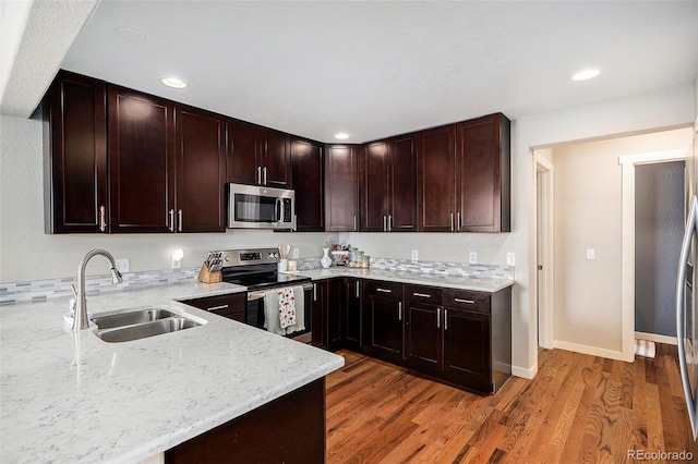 kitchen with a sink, appliances with stainless steel finishes, light stone counters, and light wood-style floors