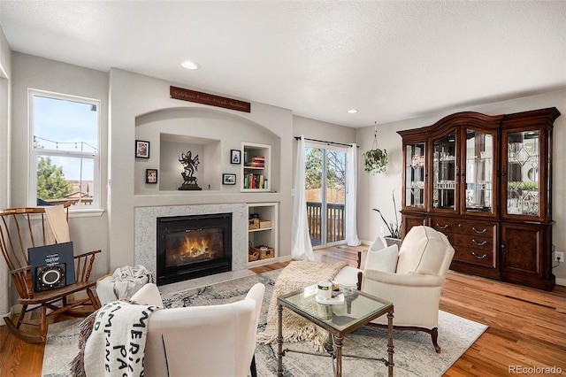 living room featuring a premium fireplace, light wood-type flooring, built in shelves, and a textured ceiling