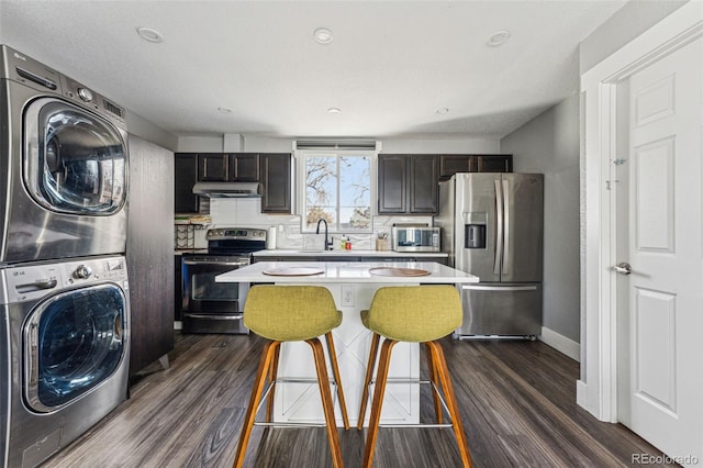 kitchen featuring stacked washer and clothes dryer, light countertops, appliances with stainless steel finishes, a kitchen island, and under cabinet range hood