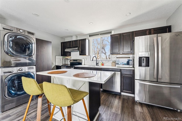 kitchen featuring stacked washer and dryer, a sink, light countertops, appliances with stainless steel finishes, and dark brown cabinets