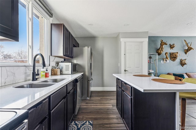 kitchen with a breakfast bar, dark wood finished floors, light countertops, stainless steel dishwasher, and a sink