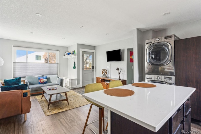 kitchen featuring stacked washer and dryer, open floor plan, wood finished floors, light countertops, and a textured ceiling