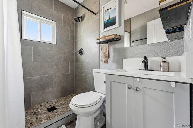 full bath with toilet, a tile shower, and vanity