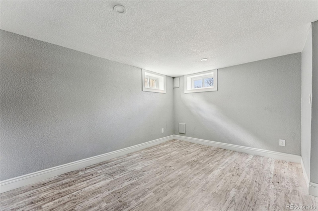 below grade area featuring a textured ceiling, a textured wall, wood finished floors, and baseboards