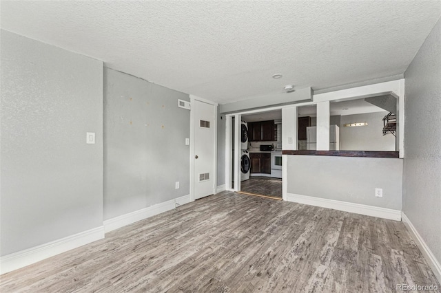 unfurnished room with a textured ceiling, wood finished floors, visible vents, and baseboards