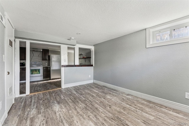 unfurnished living room with visible vents, baseboards, a textured wall, wood finished floors, and a textured ceiling