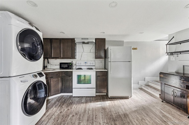 kitchen with white appliances, a sink, stacked washer / drying machine, dark brown cabinets, and light wood-type flooring