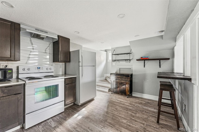 kitchen featuring dark brown cabinets, white appliances, dark wood-style flooring, and baseboards