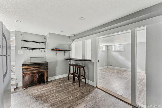 interior space featuring a textured ceiling, wood finished floors, baseboards, freestanding refrigerator, and a kitchen bar