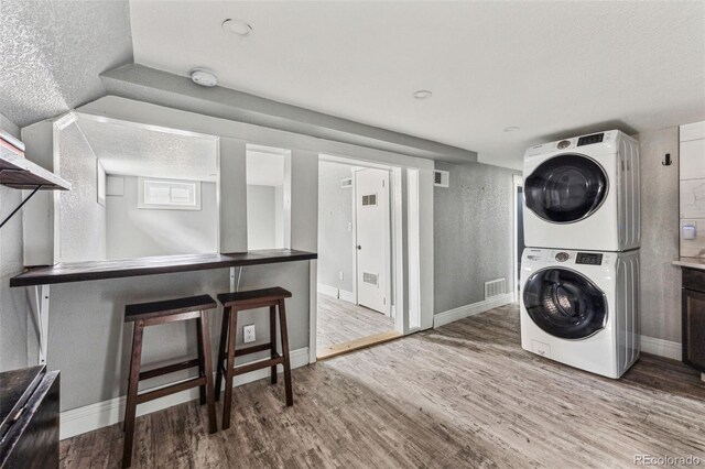 clothes washing area with laundry area, visible vents, stacked washing maching and dryer, and wood finished floors