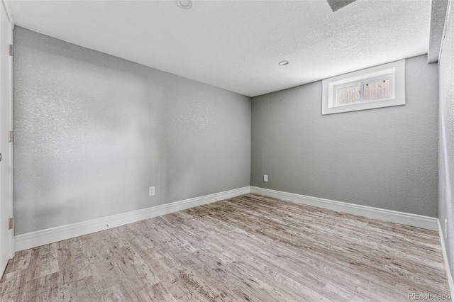 spare room featuring a textured ceiling, baseboards, wood finished floors, and a textured wall