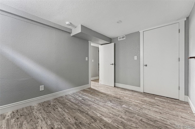 unfurnished bedroom featuring baseboards, visible vents, a textured wall, wood finished floors, and a textured ceiling