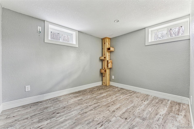 basement with a textured ceiling, baseboards, wood finished floors, and a textured wall