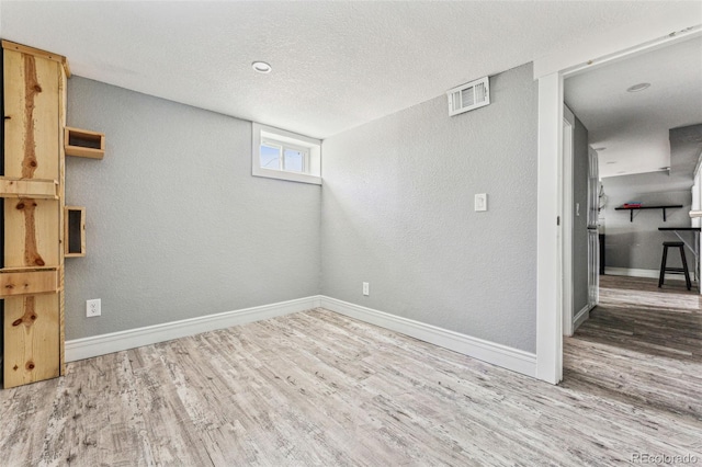 interior space with a textured ceiling, wood finished floors, visible vents, and baseboards