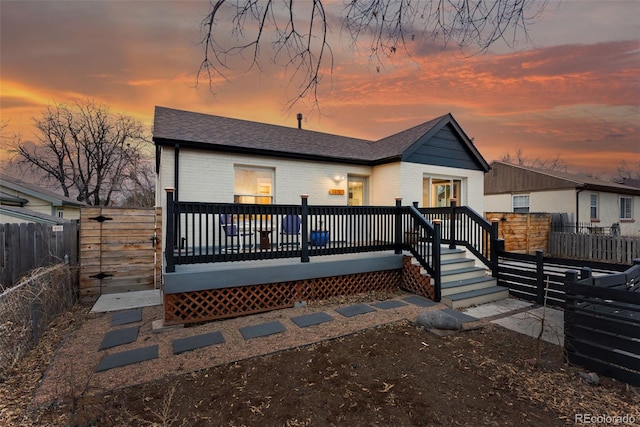 view of front of house with a shingled roof, fence, a deck, and brick siding