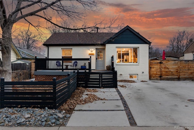 bungalow-style house with a fenced front yard, brick siding, and a deck