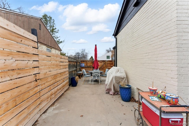 view of side of property featuring a patio, outdoor dining space, a fenced backyard, and brick siding