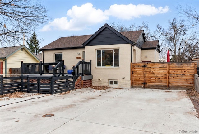 view of front of property featuring brick siding, a shingled roof, a gate, fence, and a deck