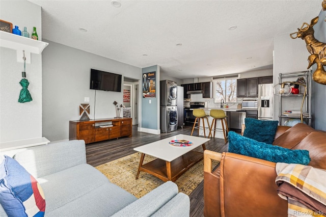 living room with dark wood-type flooring, stacked washer / drying machine, a textured ceiling, and baseboards