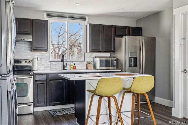 kitchen with a sink, light countertops, appliances with stainless steel finishes, range hood, and dark wood-style floors