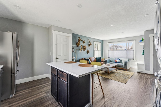 kitchen with a breakfast bar, freestanding refrigerator, dark wood-style flooring, and light countertops