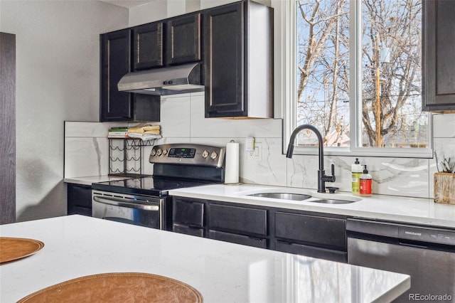 kitchen with stainless steel appliances, tasteful backsplash, light countertops, a sink, and under cabinet range hood