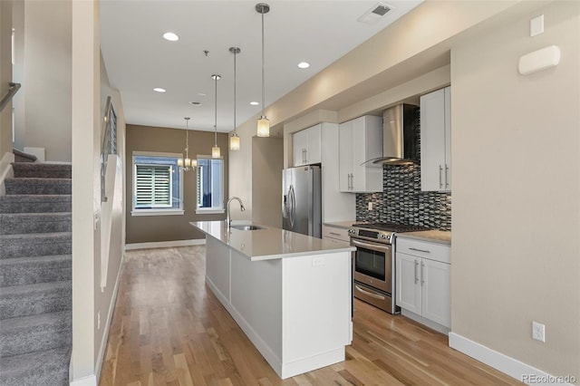 kitchen featuring wall chimney range hood, white cabinetry, appliances with stainless steel finishes, and a center island with sink