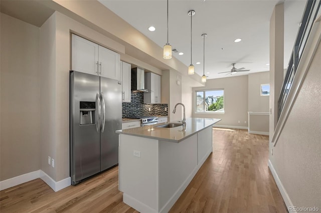 kitchen with appliances with stainless steel finishes, sink, wall chimney exhaust hood, white cabinets, and a kitchen island with sink