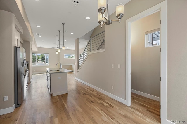 kitchen with an island with sink, white cabinetry, decorative light fixtures, stainless steel fridge, and sink