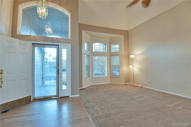 entryway featuring carpet flooring, a towering ceiling, and ceiling fan with notable chandelier