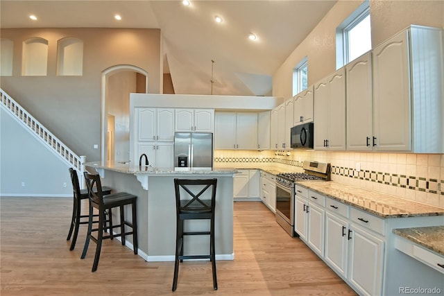 kitchen featuring light stone countertops, stainless steel appliances, a kitchen breakfast bar, a towering ceiling, and a center island with sink