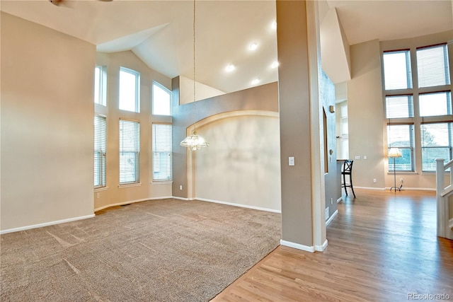 unfurnished room with hardwood / wood-style flooring, a towering ceiling, and an inviting chandelier