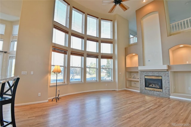 unfurnished living room with light hardwood / wood-style flooring, ceiling fan, built in features, a fireplace, and a towering ceiling