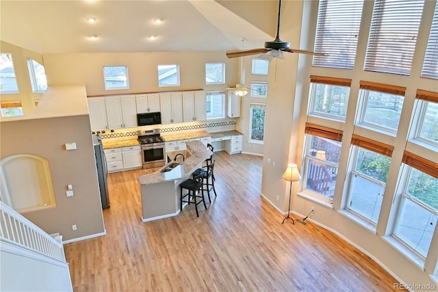 kitchen with stainless steel appliances, a towering ceiling, a breakfast bar area, decorative backsplash, and white cabinets