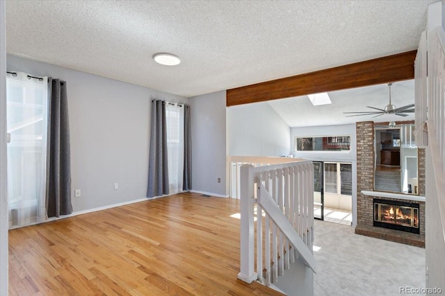 empty room with a fireplace, a textured ceiling, baseboards, and wood finished floors