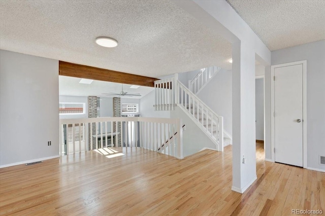 empty room featuring beamed ceiling, a textured ceiling, wood finished floors, baseboards, and ceiling fan