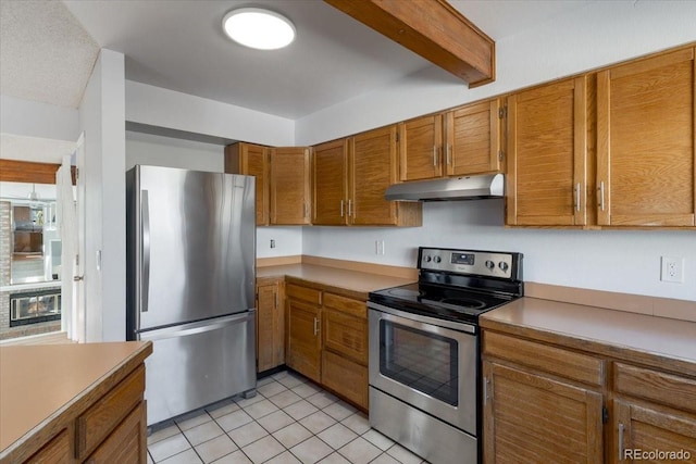 kitchen with under cabinet range hood, beamed ceiling, light tile patterned floors, appliances with stainless steel finishes, and brown cabinetry