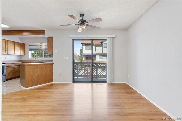 unfurnished living room featuring light wood-style flooring, a sink, a textured ceiling, baseboards, and ceiling fan