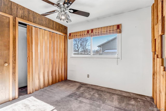 unfurnished bedroom with wooden walls, ceiling fan, carpet flooring, and a closet