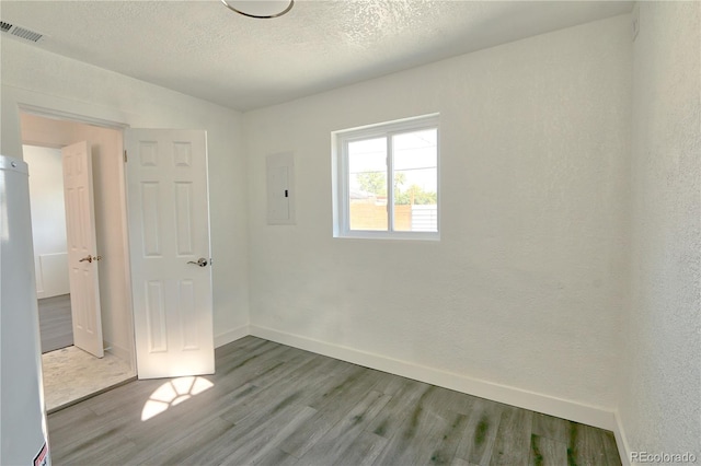 spare room with light hardwood / wood-style floors, a textured ceiling, and electric panel