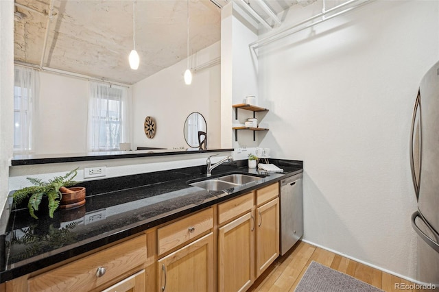 kitchen with light wood-style flooring, appliances with stainless steel finishes, dark stone countertops, pendant lighting, and a sink