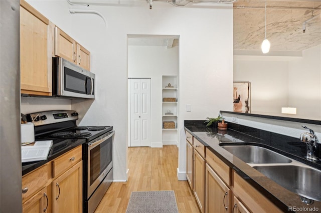 kitchen featuring appliances with stainless steel finishes, dark stone countertops, hanging light fixtures, light wood-style floors, and a sink