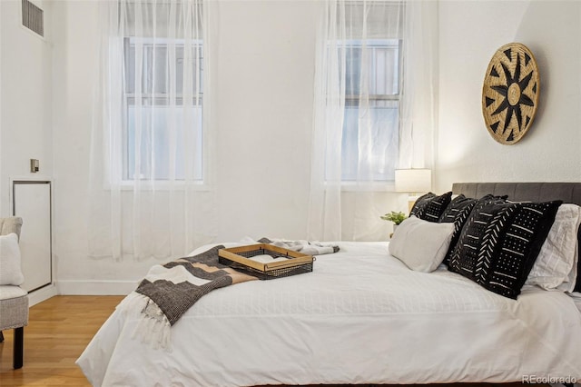 bedroom featuring multiple windows, visible vents, baseboards, and wood finished floors