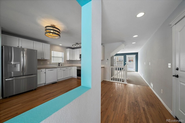 kitchen featuring track lighting, white cabinets, sink, appliances with stainless steel finishes, and dark hardwood / wood-style flooring