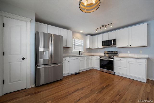 kitchen with appliances with stainless steel finishes, dark hardwood / wood-style flooring, white cabinetry, and sink