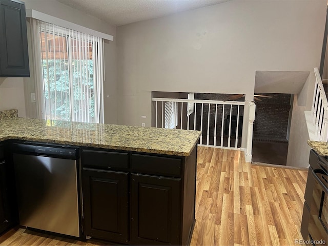 kitchen featuring a textured ceiling, light hardwood / wood-style flooring, stainless steel dishwasher, and light stone counters